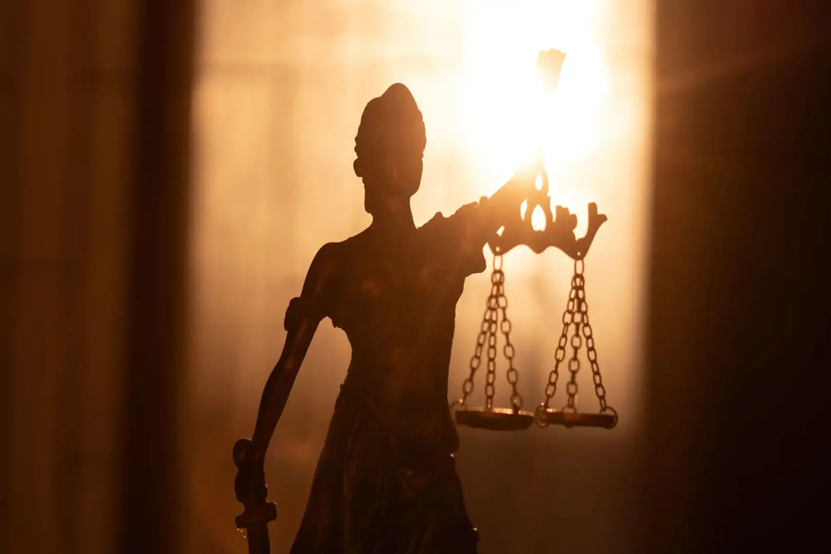 Silhouette of Lady Justice holding scales against bright sunlight.