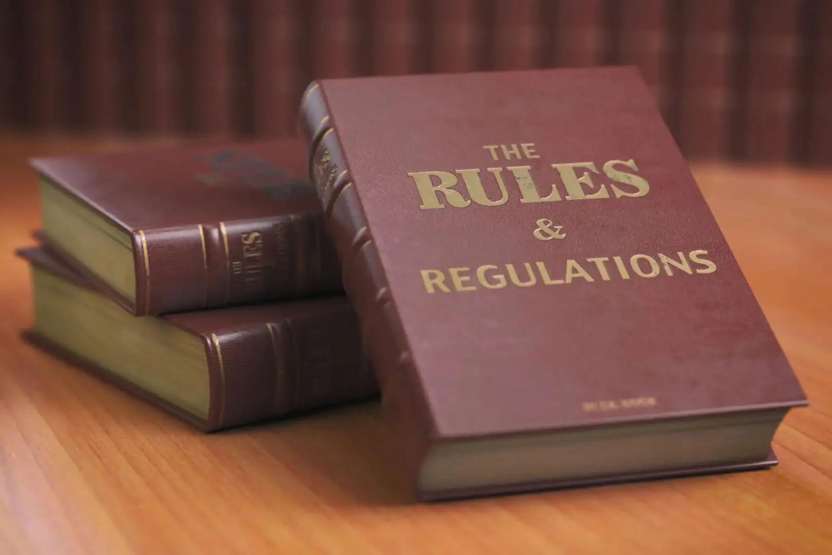 Stack of books titled 'The Rules & Regulations' on a wooden surface.